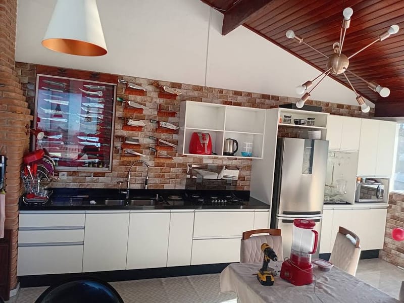 Cozinha planejada com armários brancos, bancada em granito preto, nichos abertos e adega de vinhos embutida em parede de tijolinho